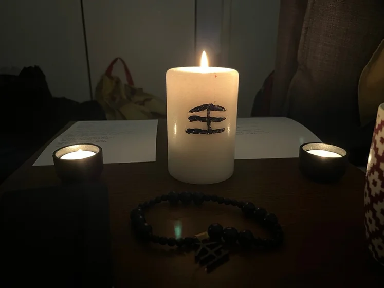 Ritual setup: Sacrifice book, prayer candles, the sacrifice candle in the center showing her holy sign, my prayer beads in front, and a cup of cocoa. Two pages written with a typewriter in the background.