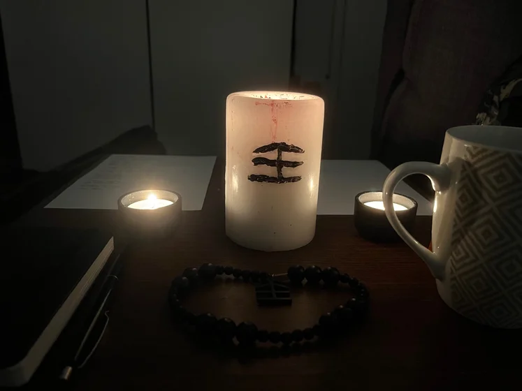 Ritual setup: Sacrifice book, prayer candles, the sacrifice candle in the center showing her holy sign, my prayer beads in front, and a cup of cocoa. Two pages written with a typewriter in the background.