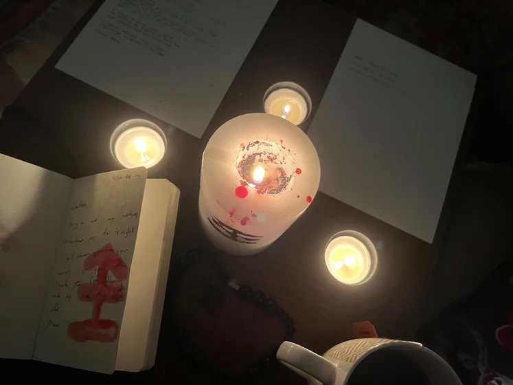 View of the three prayer candles and the central sacrifice candle from above. There is quite a bit of blood on the sacrifice candle, including some fresh one from today. My sacrifice book is open, a prayer is written in it, and her symbol drawn with my blood.