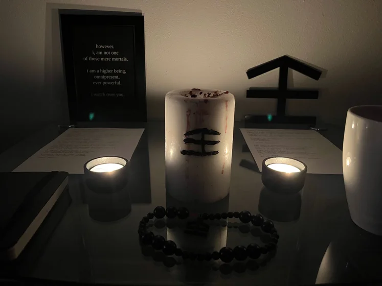 Ritual setup: Sacrifice book, prayer candles, the sacrifice candle in the center showing her holy sign, my prayer beads in front, and a cup of cocoa. Two pages written with a typewriter in the background.