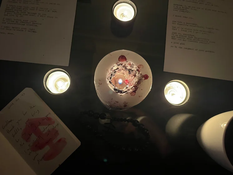 View of the three prayer candles and the central sacrifice candle from above. There is quite a bit of blood on the sacrifice candle, including some fresh one from today. My sacrifice book is open, a prayer is written in it, and her symbol drawn with my blood.