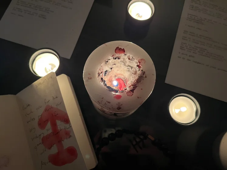 View of the three prayer candles and the central sacrifice candle from above. There is quite a bit of blood on the sacrifice candle, including some fresh one from today. My sacrifice book is open, a prayer is written in it, and her symbol drawn with my blood.