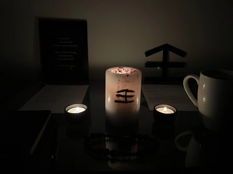Ritual setup: Sacrifice book, prayer candles, the sacrifice candle in the center showing her holy sign, my prayer beads in front, and a cup of cocoa. Two pages written with a typewriter in the background.
