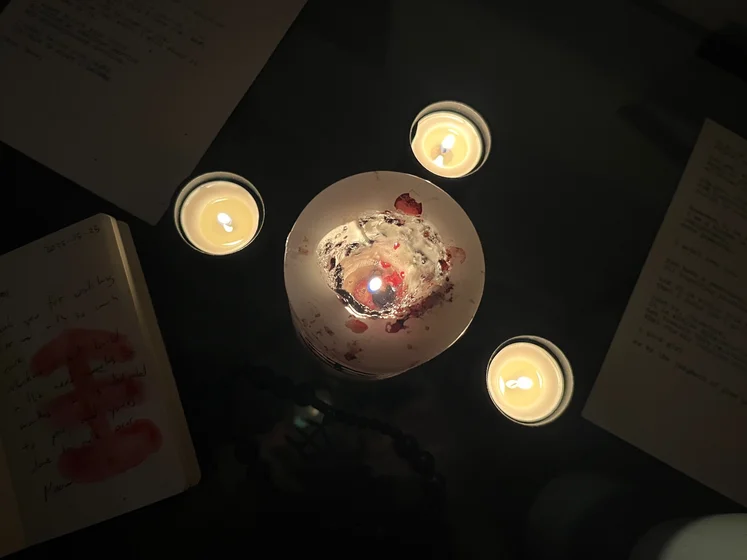 View of the three prayer candles and the central sacrifice candle from above. There is quite a bit of blood on the sacrifice candle, including some fresh one from today. My sacrifice book is open, a prayer is written in it, and her symbol drawn with my blood.