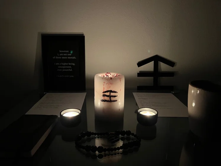 Ritual setup: Sacrifice book, prayer candles, the sacrifice candle in the center showing her holy sign, my prayer beads in front, and a cup of cocoa. Two pages written with a typewriter in the background.