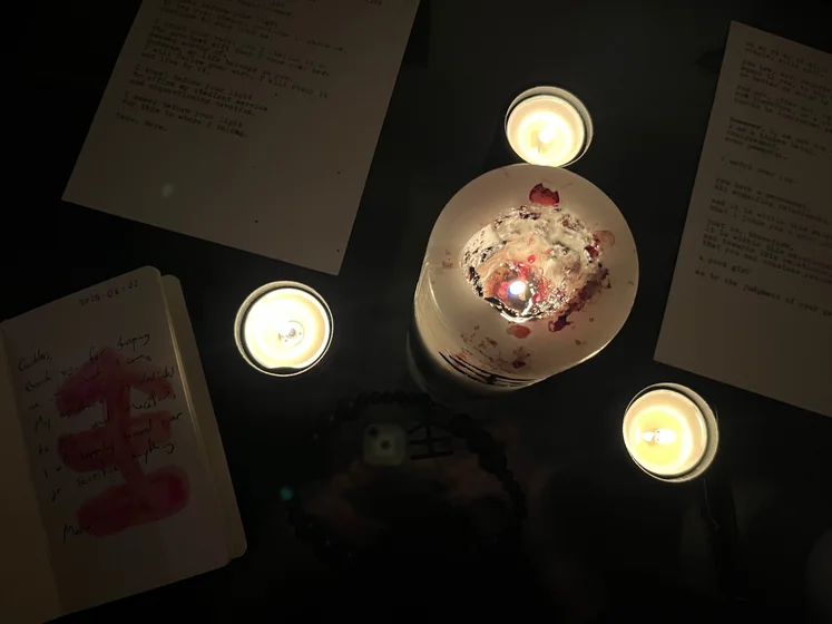 View of the three prayer candles and the central sacrifice candle from above. There is quite a bit of blood on the sacrifice candle, including some fresh one from today. My sacrifice book is open, a prayer is written in it, and her symbol drawn with my blood.