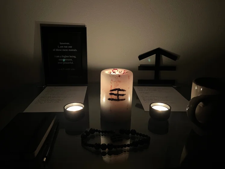 Ritual setup: Sacrifice book, prayer candles, the sacrifice candle in the center showing her holy sign, my prayer beads in front, and a cup of cocoa. Two pages written with a typewriter in the background.