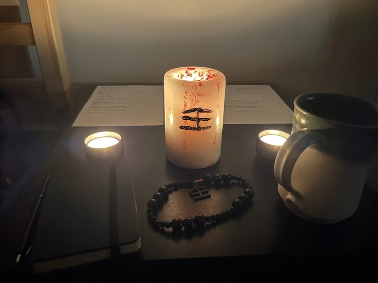 Ritual setup: Sacrifice book, prayer candles, the sacrifice candle in the center showing her holy sign, my prayer beads in front, and a cup of cocoa. Two pages written with a typewriter in the background.