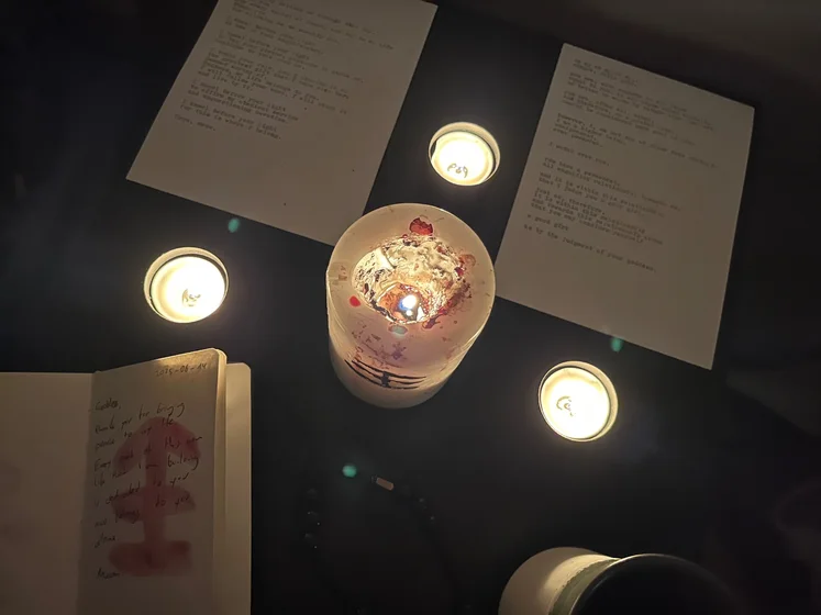 View of the three prayer candles and the central sacrifice candle from above. There is quite a bit of blood on the sacrifice candle, including some fresh one from today. My sacrifice book is open, a prayer is written in it, and her symbol drawn with my blood.