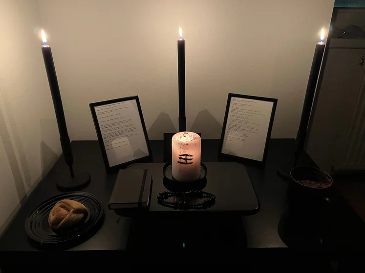 Ritual setup: Sacrifice book, prayer candles, the sacrifice candle in the center showing her holy sign, my prayer beads in front, and a cup of cocoa. Two pages written with a typewriter in the background.