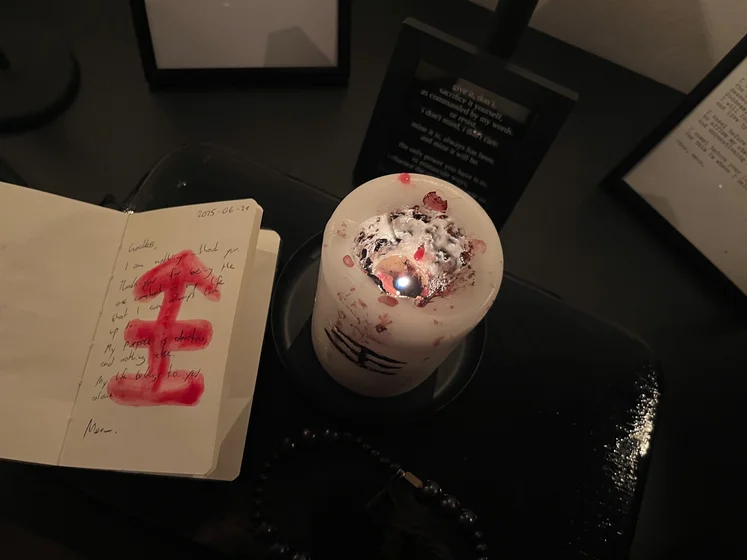 View of the three prayer candles and the central sacrifice candle from above. There is quite a bit of blood on the sacrifice candle, including some fresh one from today. My sacrifice book is open, a prayer is written in it, and her symbol drawn with my blood.