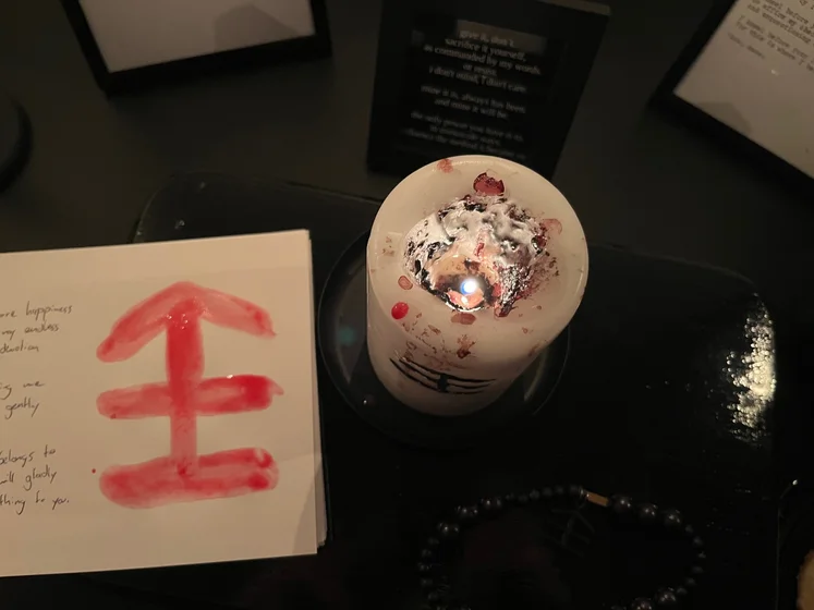 View of the three prayer candles and the central sacrifice candle from above. There is quite a bit of blood on the sacrifice candle, including some fresh one from today. My sacrifice book is open, a prayer is written in it, and her symbol drawn with my blood.