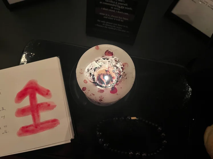 View of the three prayer candles and the central sacrifice candle from above. There is quite a bit of blood on the sacrifice candle, including some fresh one from today. My sacrifice book is open, a prayer is written in it, and her symbol drawn with my blood.