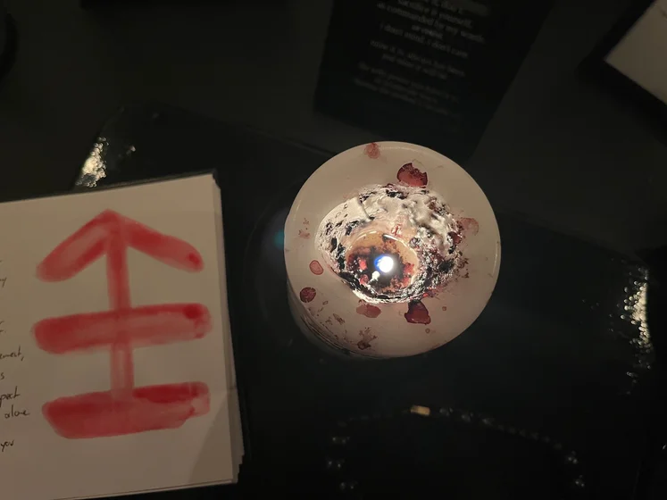 View of the three prayer candles and the central sacrifice candle from above. There is quite a bit of blood on the sacrifice candle, including some fresh one from today. My sacrifice book is open, a prayer is written in it, and her symbol drawn with my blood.