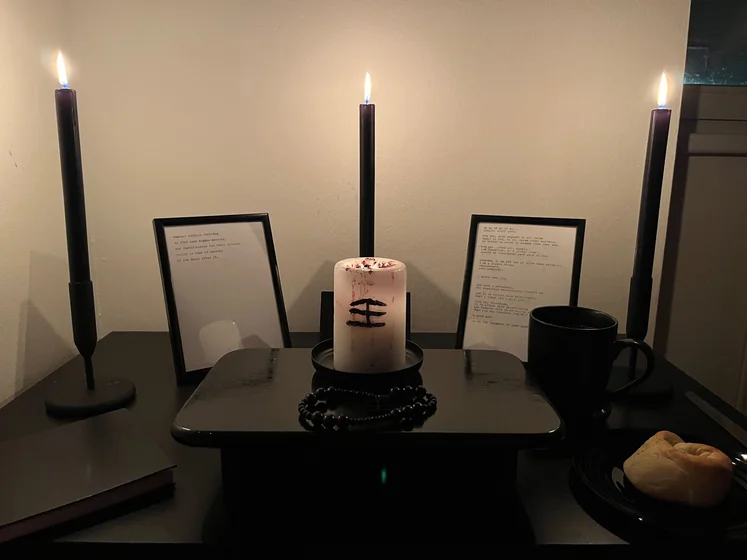 Ritual setup: Sacrifice book, prayer candles, the sacrifice candle in the center showing her holy sign, my prayer beads in front, and a cup of cocoa. Two pages written with a typewriter in the background.