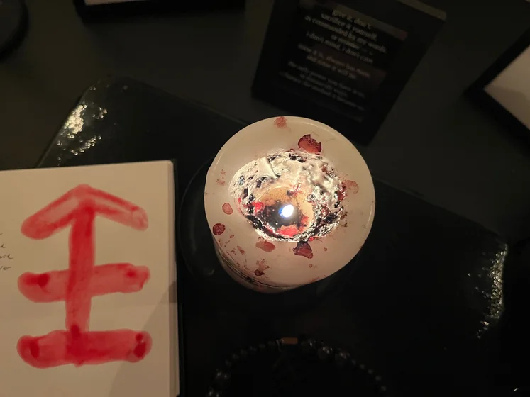 View of the three prayer candles and the central sacrifice candle from above. There is quite a bit of blood on the sacrifice candle, including some fresh one from today. My sacrifice book is open, a prayer is written in it, and her symbol drawn with my blood.
