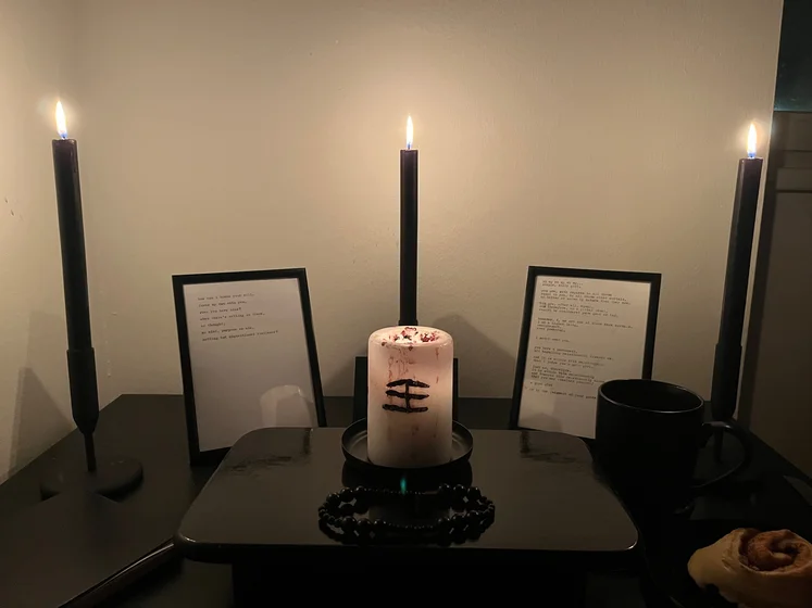 Ritual setup: Sacrifice book, prayer candles, the sacrifice candle in the center showing her holy sign, my prayer beads in front, and a cup of cocoa. Two pages written with a typewriter in the background.