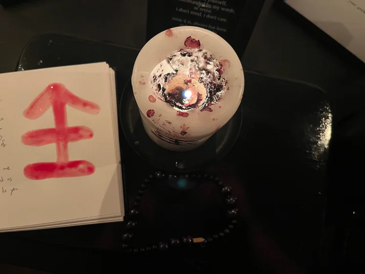 View of the three prayer candles and the central sacrifice candle from above. There is quite a bit of blood on the sacrifice candle, including some fresh one from today. My sacrifice book is open, a prayer is written in it, and her symbol drawn with my blood.