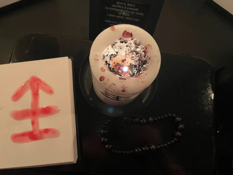 View of the three prayer candles and the central sacrifice candle from above. There is quite a bit of blood on the sacrifice candle, including some fresh one from today. My sacrifice book is open, a prayer is written in it, and her symbol drawn with my blood.