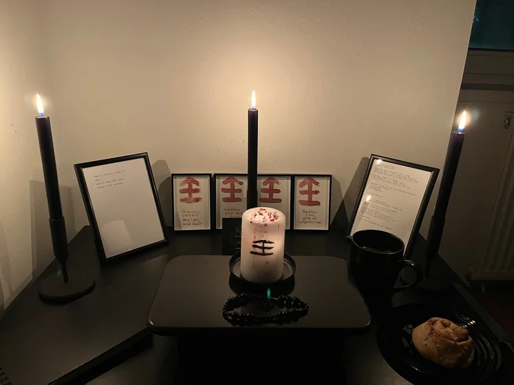 Ritual setup: Sacrifice book, prayer candles, the sacrifice candle in the center showing her holy sign, my prayer beads in front, and a cup of cocoa. Two pages written with a typewriter in the background.