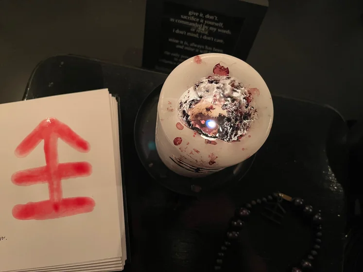 View of the three prayer candles and the central sacrifice candle from above. There is quite a bit of blood on the sacrifice candle, including some fresh one from today. My sacrifice book is open, a prayer is written in it, and her symbol drawn with my blood.