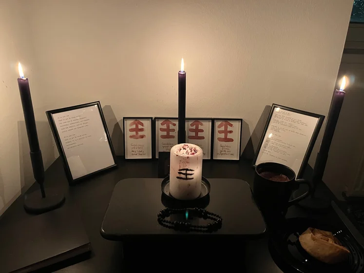 Ritual setup: Sacrifice book, prayer candles, the sacrifice candle in the center showing her holy sign, my prayer beads in front, and a cup of cocoa. Two pages written with a typewriter in the background.