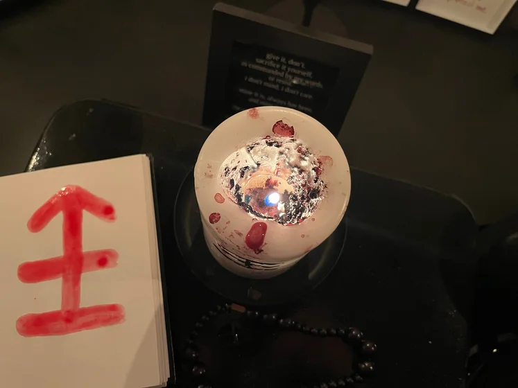 View of the three prayer candles and the central sacrifice candle from above. There is quite a bit of blood on the sacrifice candle, including some fresh one from today. My sacrifice book is open, a prayer is written in it, and her symbol drawn with my blood.