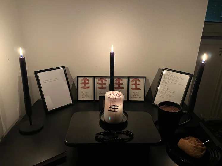 Ritual setup: Sacrifice book, prayer candles, the sacrifice candle in the center showing her holy sign, my prayer beads in front, and a cup of cocoa. Two pages written with a typewriter in the background.