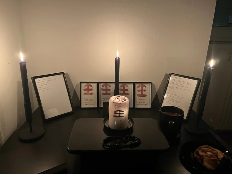 Ritual setup: Sacrifice book, prayer candles, the sacrifice candle in the center showing her holy sign, my prayer beads in front, and a cup of cocoa. Two pages written with a typewriter in the background.