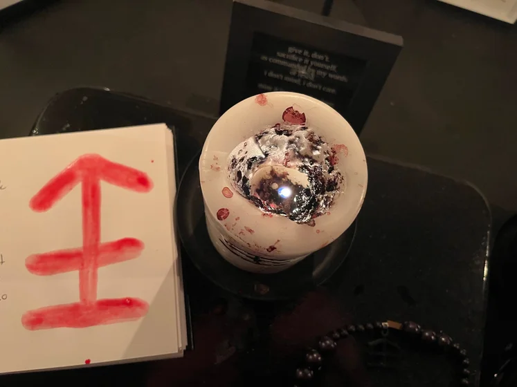 View of the three prayer candles and the central sacrifice candle from above. There is quite a bit of blood on the sacrifice candle, including some fresh one from today. My sacrifice book is open, a prayer is written in it, and her symbol drawn with my blood.