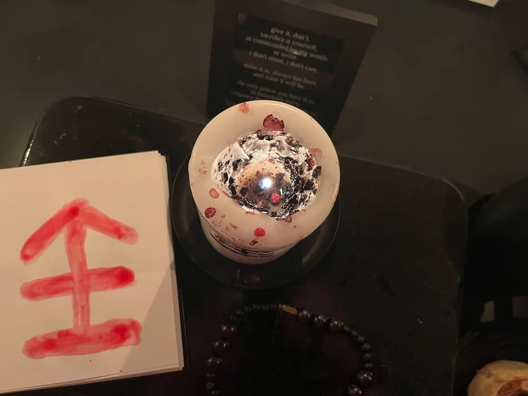 View of the three prayer candles and the central sacrifice candle from above. There is quite a bit of blood on the sacrifice candle, including some fresh one from today. My sacrifice book is open, a prayer is written in it, and her symbol drawn with my blood.