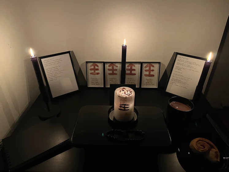 Ritual setup: Sacrifice book, prayer candles, the sacrifice candle in the center showing her holy sign, my prayer beads in front, and a cup of cocoa. Two pages written with a typewriter in the background.