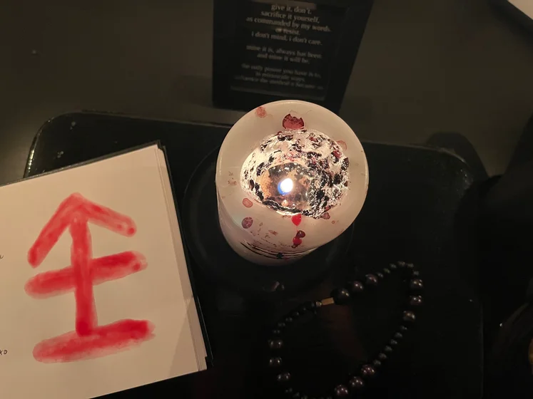 View of the three prayer candles and the central sacrifice candle from above. There is quite a bit of blood on the sacrifice candle, including some fresh one from today. My sacrifice book is open, a prayer is written in it, and her symbol drawn with my blood.