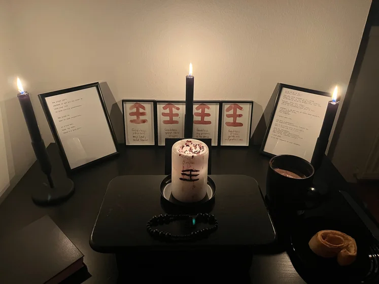 Ritual setup: Sacrifice book, prayer candles, the sacrifice candle in the center showing her holy sign, my prayer beads in front, and a cup of cocoa. Two pages written with a typewriter in the background.