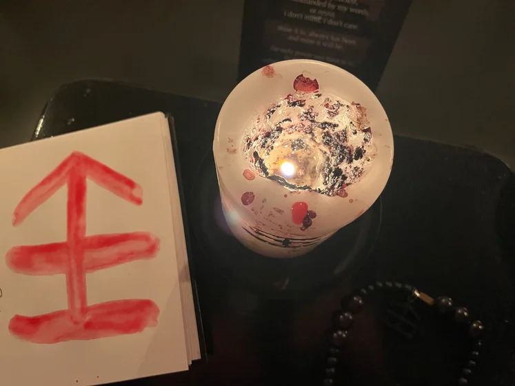 View of the three prayer candles and the central sacrifice candle from above. There is quite a bit of blood on the sacrifice candle, including some fresh one from today. My sacrifice book is open, a prayer is written in it, and her symbol drawn with my blood.