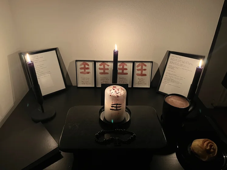Ritual setup: Sacrifice book, prayer candles, the sacrifice candle in the center showing her holy sign, my prayer beads in front, and a cup of cocoa. Two pages written with a typewriter in the background.