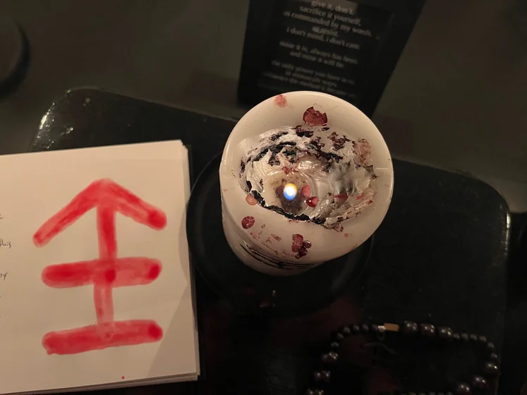 View of the three prayer candles and the central sacrifice candle from above. There is quite a bit of blood on the sacrifice candle, including some fresh one from today. My sacrifice book is open, a prayer is written in it, and her symbol drawn with my blood.