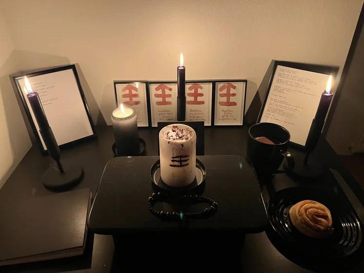 Ritual setup: Sacrifice book, prayer candles, the sacrifice candle in the center showing her holy sign, my prayer beads in front, and a cup of cocoa. Two pages written with a typewriter in the background.