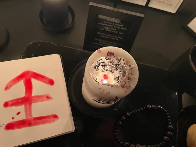 View of the three prayer candles and the central sacrifice candle from above. There is quite a bit of blood on the sacrifice candle, including some fresh one from today. My sacrifice book is open, a prayer is written in it, and her symbol drawn with my blood.