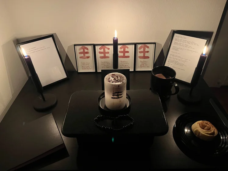 Ritual setup: Sacrifice book, prayer candles, the sacrifice candle in the center showing her holy sign, my prayer beads in front, and a cup of cocoa. Two pages written with a typewriter in the background.