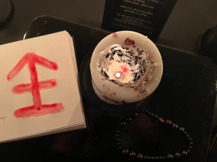 View of the three prayer candles and the central sacrifice candle from above. There is quite a bit of blood on the sacrifice candle, including some fresh one from today. My sacrifice book is open, a prayer is written in it, and her symbol drawn with my blood.