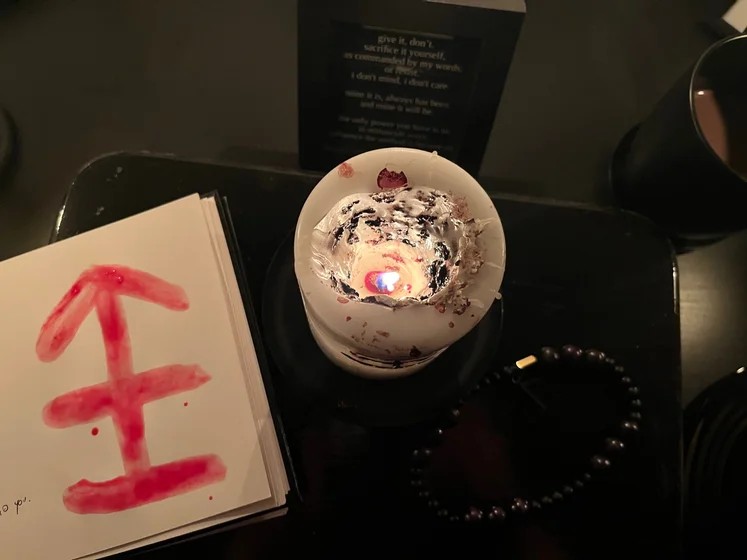 View of the three prayer candles and the central sacrifice candle from above. There is quite a bit of blood on the sacrifice candle, including some fresh one from today. My sacrifice book is open, a prayer is written in it, and her symbol drawn with my blood.