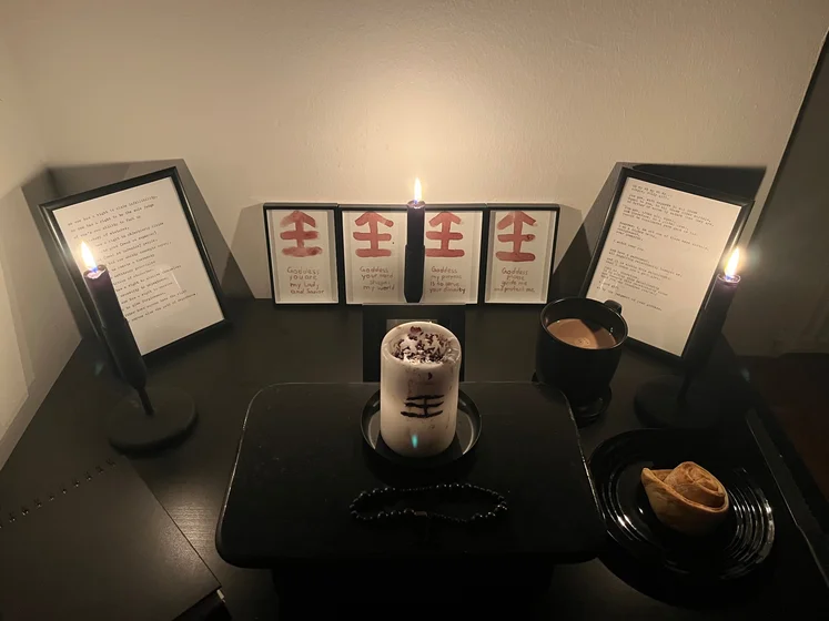 Ritual setup: Sacrifice book, prayer candles, the sacrifice candle in the center showing her holy sign, my prayer beads in front, and a cup of cocoa. Two pages written with a typewriter in the background.