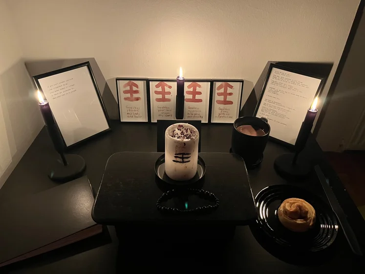Ritual setup: Sacrifice book, prayer candles, the sacrifice candle in the center showing her holy sign, my prayer beads in front, and a cup of cocoa. Two pages written with a typewriter in the background.