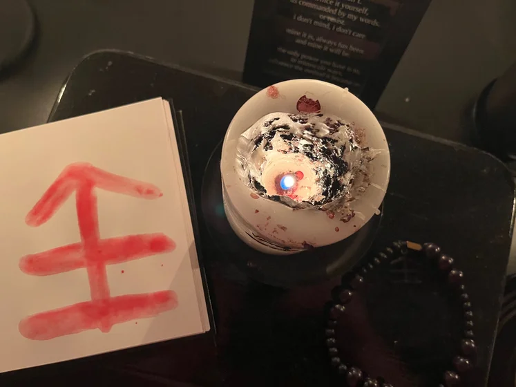 View of the three prayer candles and the central sacrifice candle from above. There is quite a bit of blood on the sacrifice candle, including some fresh one from today. My sacrifice book is open, a prayer is written in it, and her symbol drawn with my blood.
