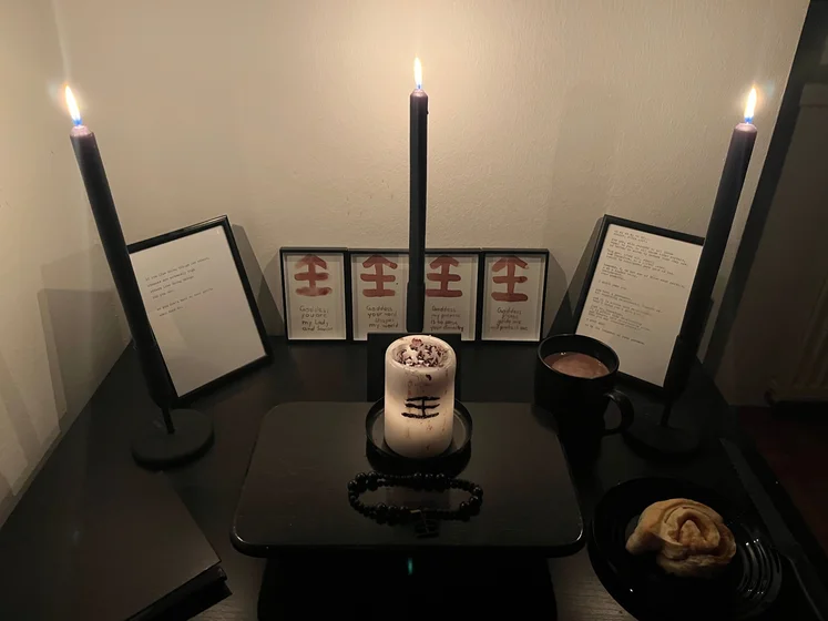 Ritual setup: Sacrifice book, prayer candles, the sacrifice candle in the center showing her holy sign, my prayer beads in front, and a cup of cocoa. Two pages written with a typewriter in the background.