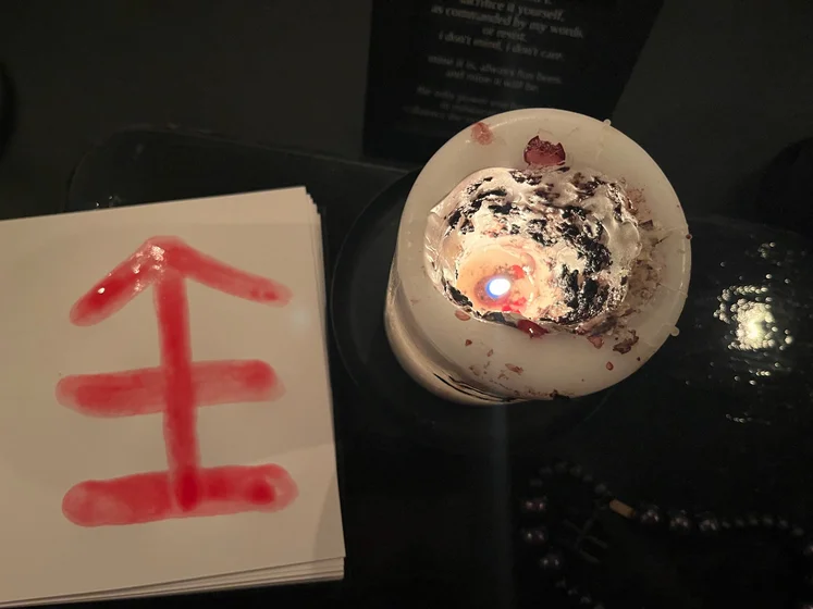 View of the three prayer candles and the central sacrifice candle from above. There is quite a bit of blood on the sacrifice candle, including some fresh one from today. My sacrifice book is open, a prayer is written in it, and her symbol drawn with my blood.