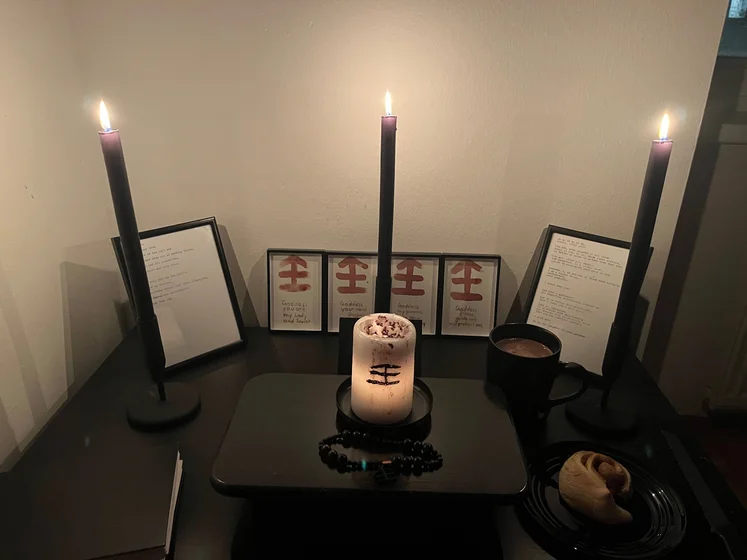 Ritual setup: Sacrifice book, prayer candles, the sacrifice candle in the center showing her holy sign, my prayer beads in front, and a cup of cocoa. Two pages written with a typewriter in the background.