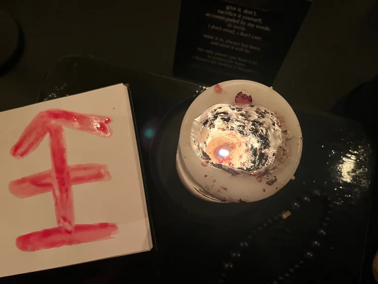 View of the three prayer candles and the central sacrifice candle from above. There is quite a bit of blood on the sacrifice candle, including some fresh one from today. My sacrifice book is open, a prayer is written in it, and her symbol drawn with my blood.