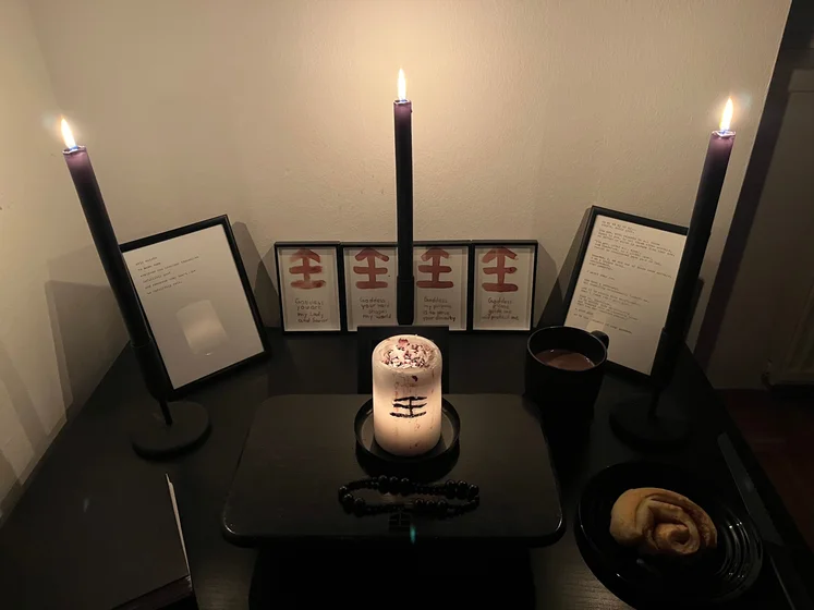 Ritual setup: Sacrifice book, prayer candles, the sacrifice candle in the center showing her holy sign, my prayer beads in front, and a cup of cocoa. Two pages written with a typewriter in the background.